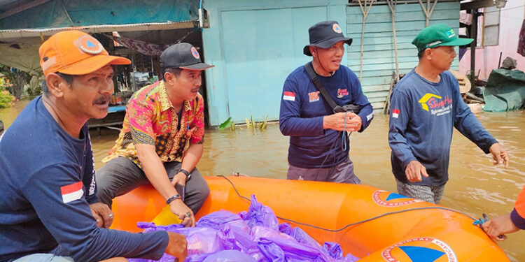 BAGIKAN BANTUAN - Kepala BPBD Tapin H Raniansyah membagikan bantuan logistik kepada korban terdampak banjir di Desa Parigi Simbar, Kecamatan Bakarangan dengan menggunakan perahu karet dan menyambangi warga dari rumah ke rumah, Kamis (11/1).