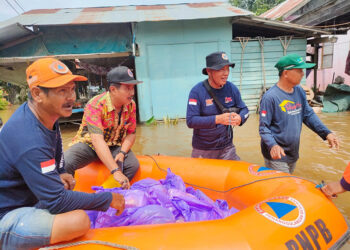 BAGIKAN BANTUAN - Kepala BPBD Tapin H Raniansyah membagikan bantuan logistik kepada korban terdampak banjir di Desa Parigi Simbar, Kecamatan Bakarangan dengan menggunakan perahu karet dan menyambangi warga dari rumah ke rumah, Kamis (11/1).