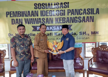 ANGGOTA DPRD Kalsel Dr H Karlie Hanafi Kalianda SH MH saat menyerahkan cinderamata berupa lambang negara Indonesia kepada Kepala Desa Anjir Pasar Kota Abriansyah.