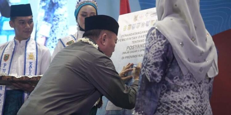 Gubernur Kalimantan Selatan, H Muhidin saat menandatangani komitmen bersama untuk menerapkan 6 standar pelayanan minimal (SPM) di Kalsel, disaksikan Ketua Tim Pembina Posyandu Provinsi Kalsel, Hj Fathul Jannah