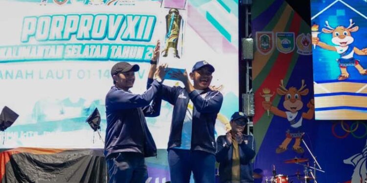 Wakil Gubernur (Wagub) Kalimantan Selatan, Hasnuryadi Sulaiman saat menyerahkan tropi bergilir juara umum Porprov Kalsel tahun 2025 diterima Bupati Tanah Laut (Tala), H Rahmat Trianto pada penutupan Porprov XII Kalsel, di Pelaihari