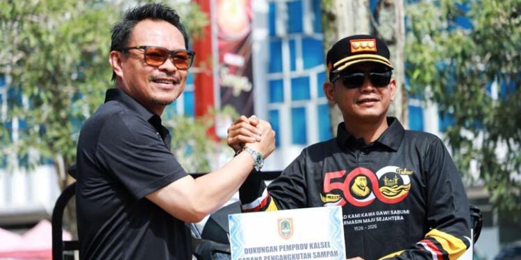Plh Sekdaprov Kalimantan Selatan, H Subhan Nor Yaumil saat menyerahkan bantuan fasilitas pengelolaan sampah dan diterima Walikota Banjarmasin, HM Yamin HR disela aksi bersih-bersih dalam rangka peringatan Hari Lingkungan Hidup Sedunia tahun 2026